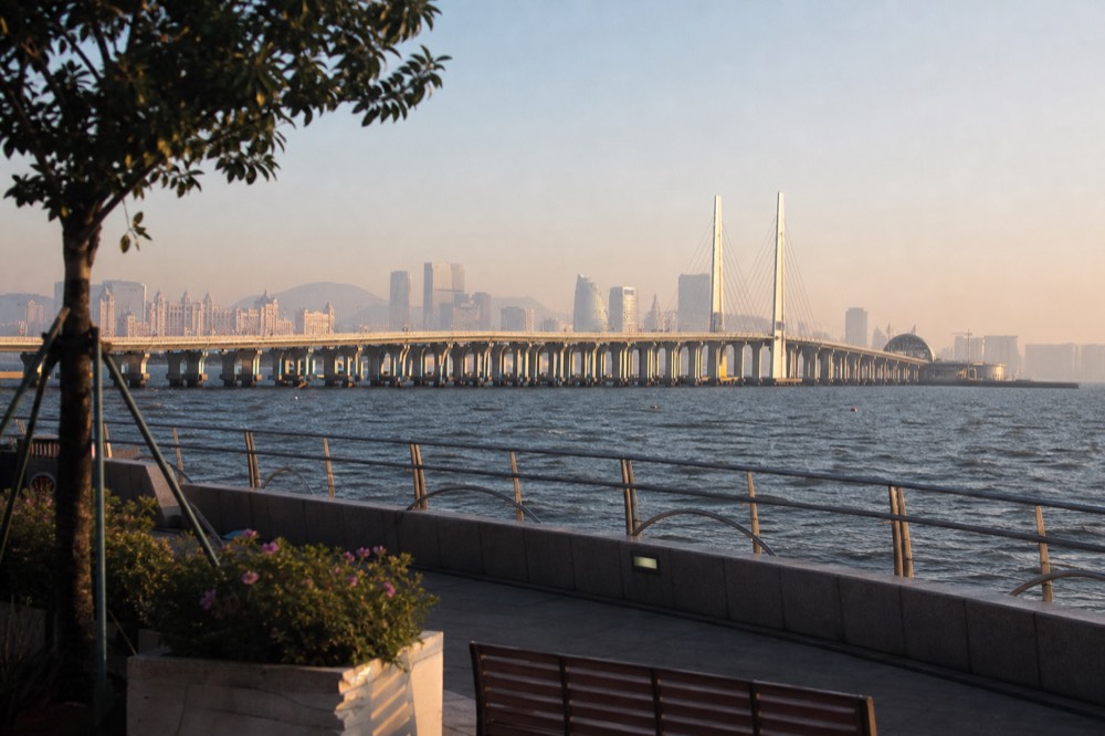 A red bridge stretching across open sea toward the Macau skyline in late afternoon light