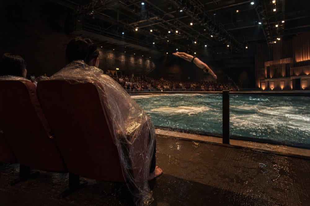 Front rows beside a deep pool stage with performers mid-dive