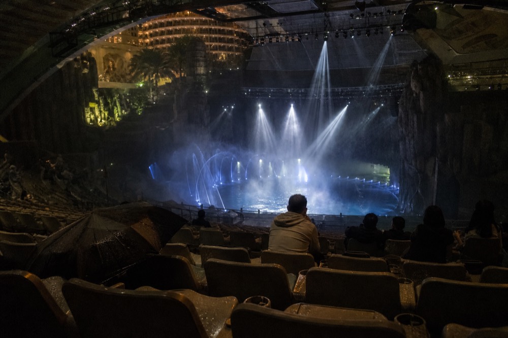 A theatre-in-the-round auditorium with a deep pool stage under show lighting