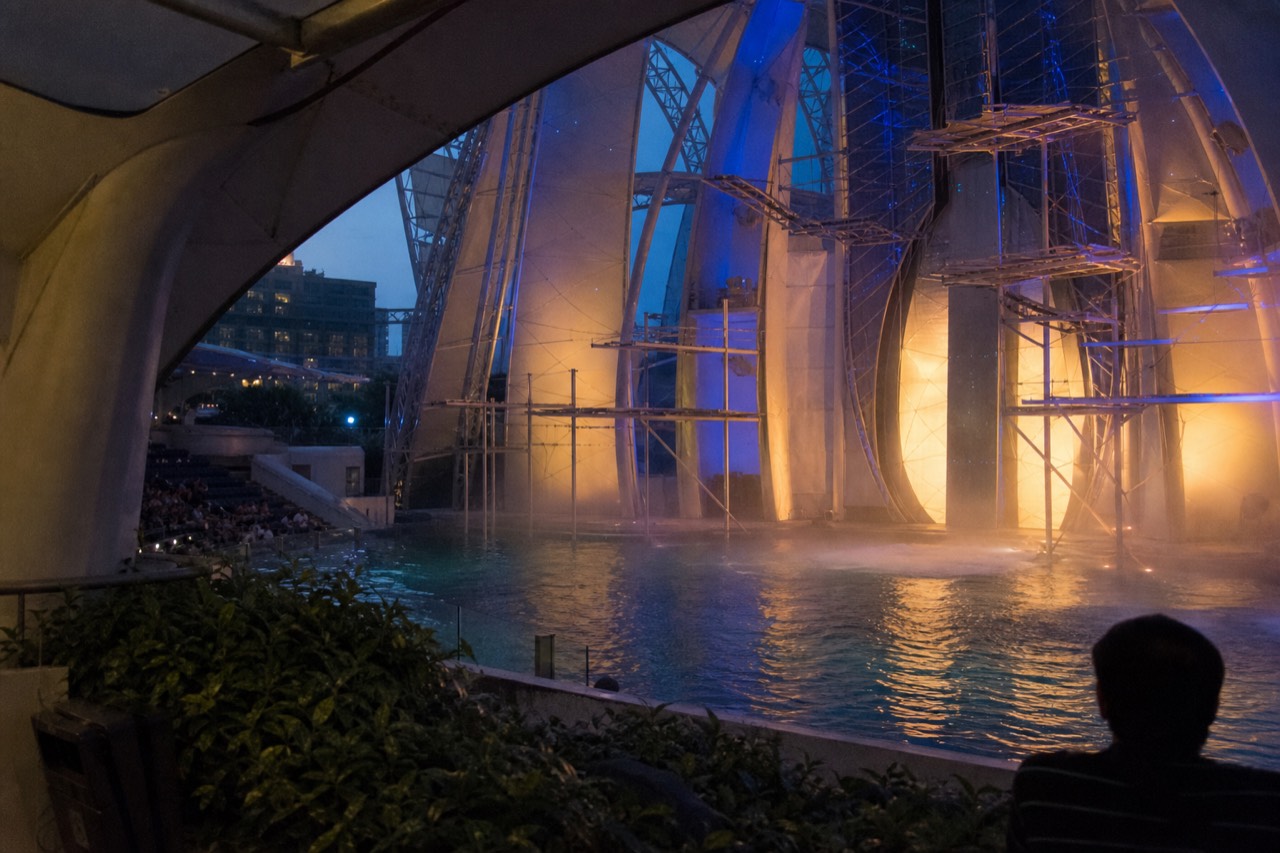 The stage and pool of a large aquatic theatre lit for an evening performance