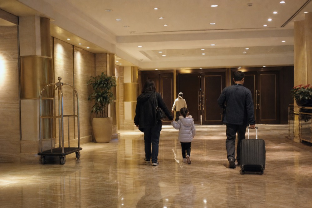 Family walking through a resort theatre foyer, a child in a light jacket holding an adult hand
