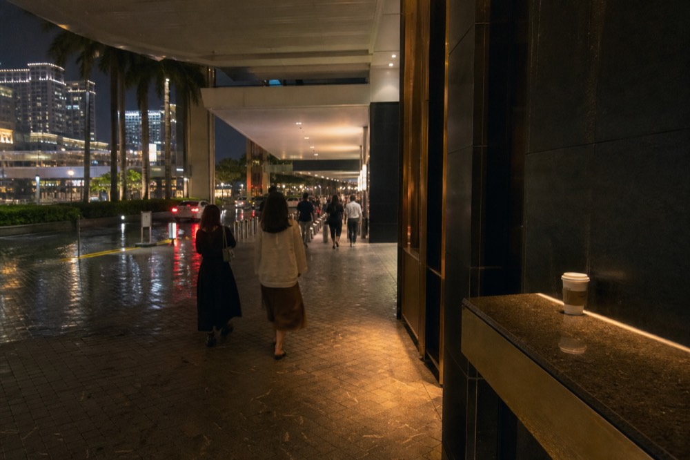 Resort corridor at night with guests walking toward transport links after a show, wet pavement reflecting lights