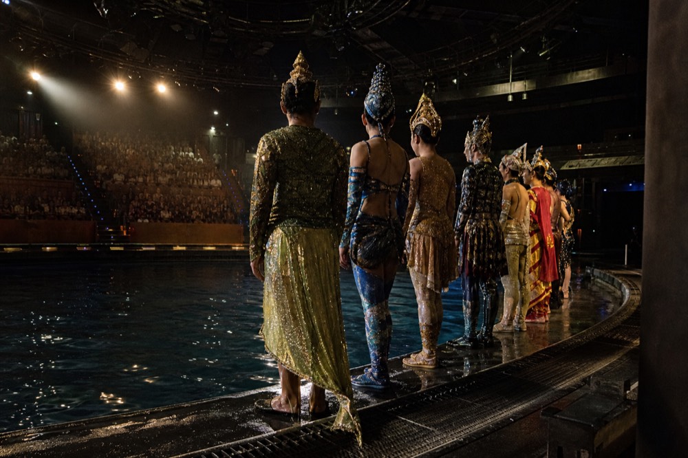 A cast of performers in elaborate costumes standing in a line on stage