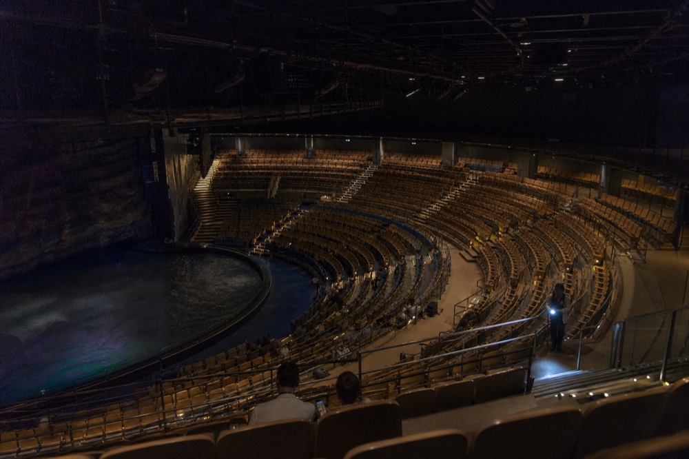 A wide view of a theatre in the round filled with tiered seating