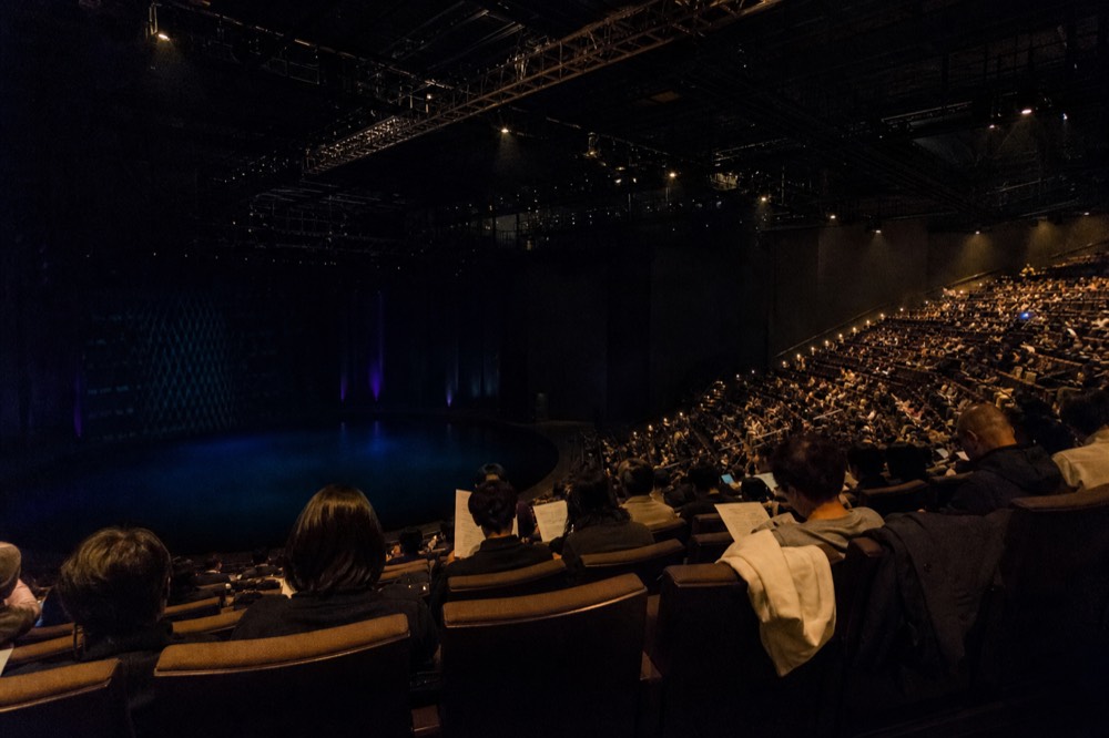 An evening audience settling into tiered theatre seating before curtain