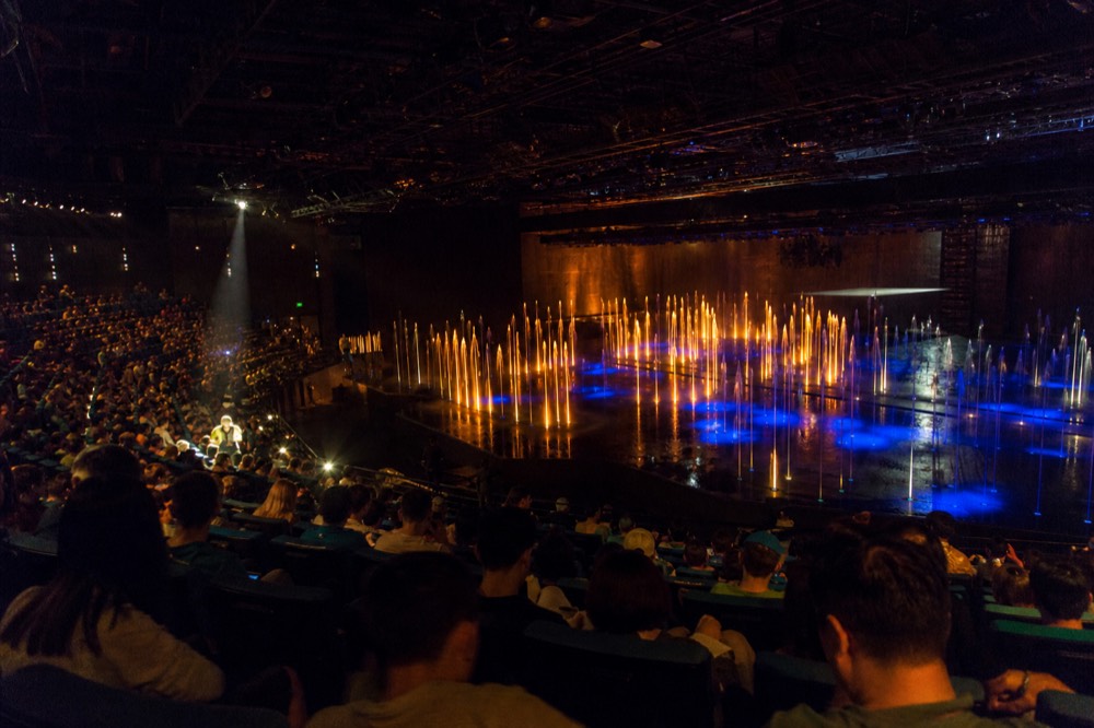 The water theatre stage lit for an evening performance with the auditorium filling