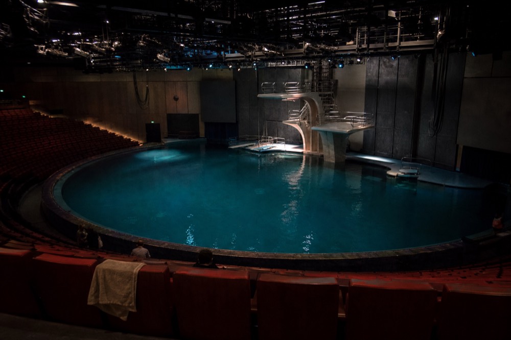 A round theatre with a deep pool stage lit before a performance