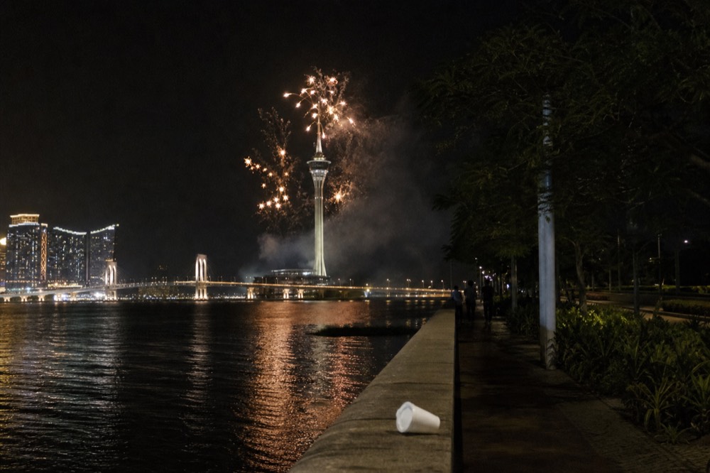 Fireworks bursting over the sea in front of a lit tower at night